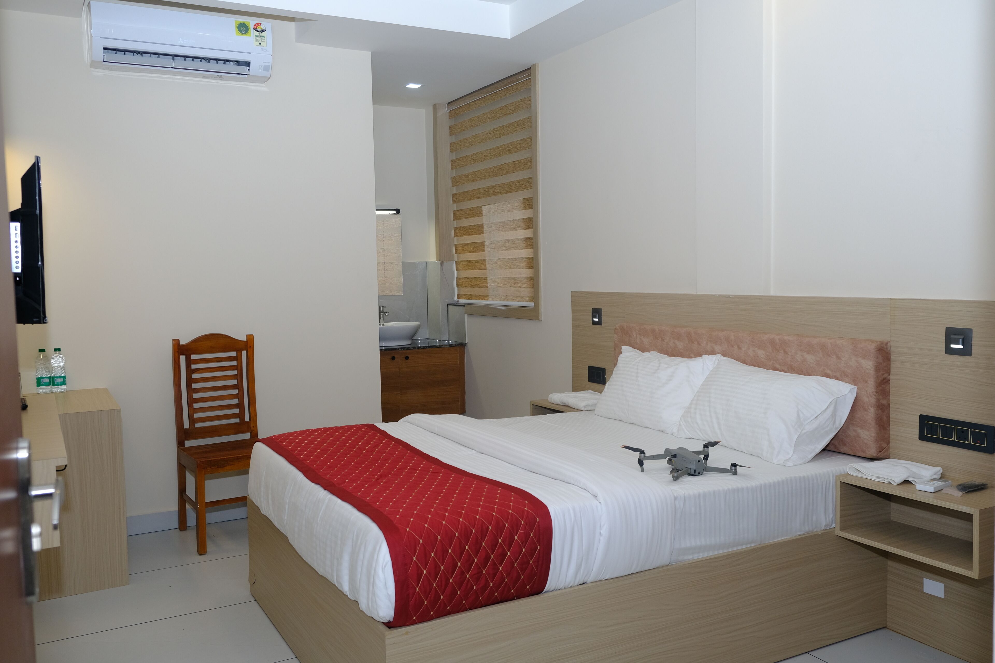 Habitació d'hotel amb llit, una petita taula de nit de fusta, escriptori, cadira, mirall i aparell d'aire condicionat.