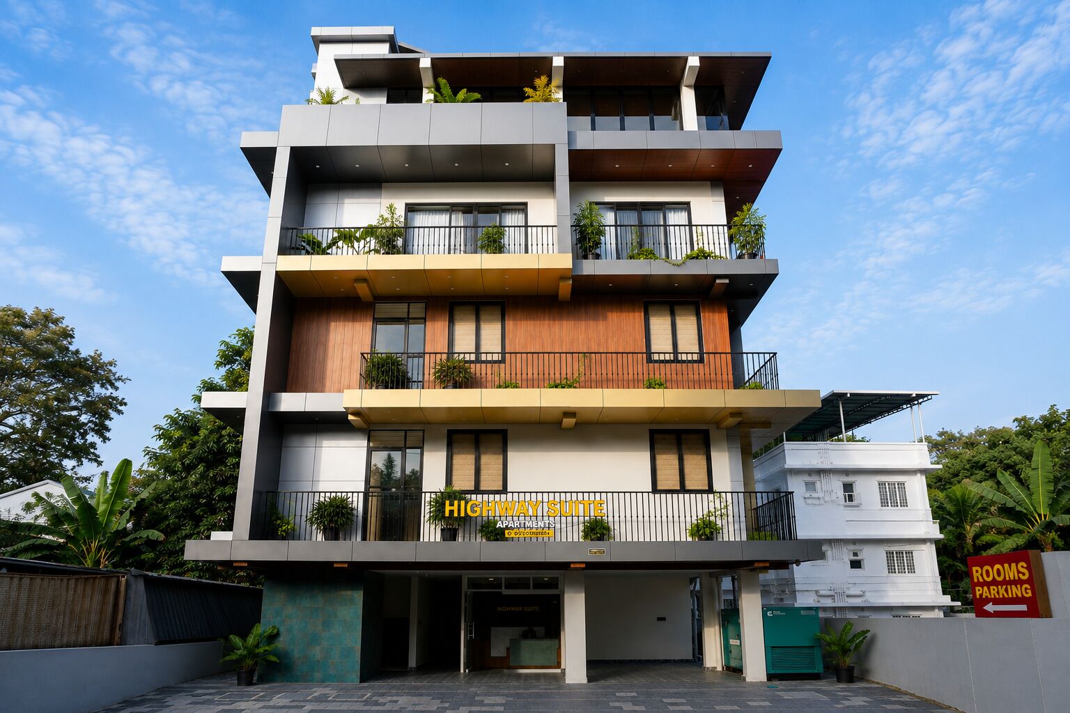 A multi-story hotel with a modern design, featuring balconies with plants, a sign indicating 'Highway Suite' apartments, and a 'Rooms Parking' sign.