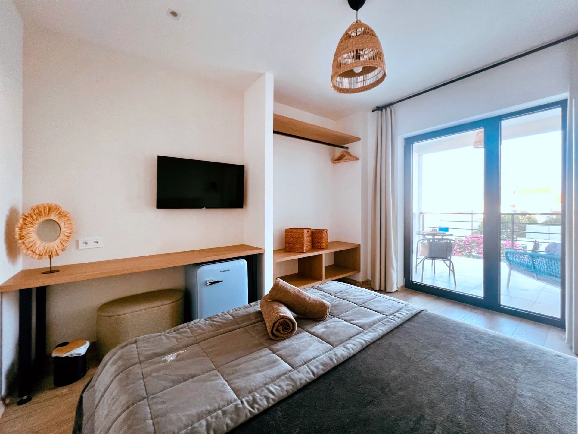 Ein modernes Schlafzimmer mit einem Bett, einem Flachbildfernseher, einem kleinen Schreibtisch und einem großen Fenster.