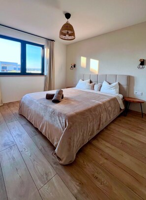 A bedroom with a large bed, wooden flooring, a window with curtains, and a hanging light fixture. - Vila Esnella – Private Pool & Panoramic Sea View (Primošten)