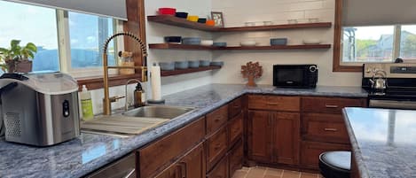 A kitchen with a built-in dishwasher, a microwave, wooden cabinets, a granite countertop, and a window with blinds.