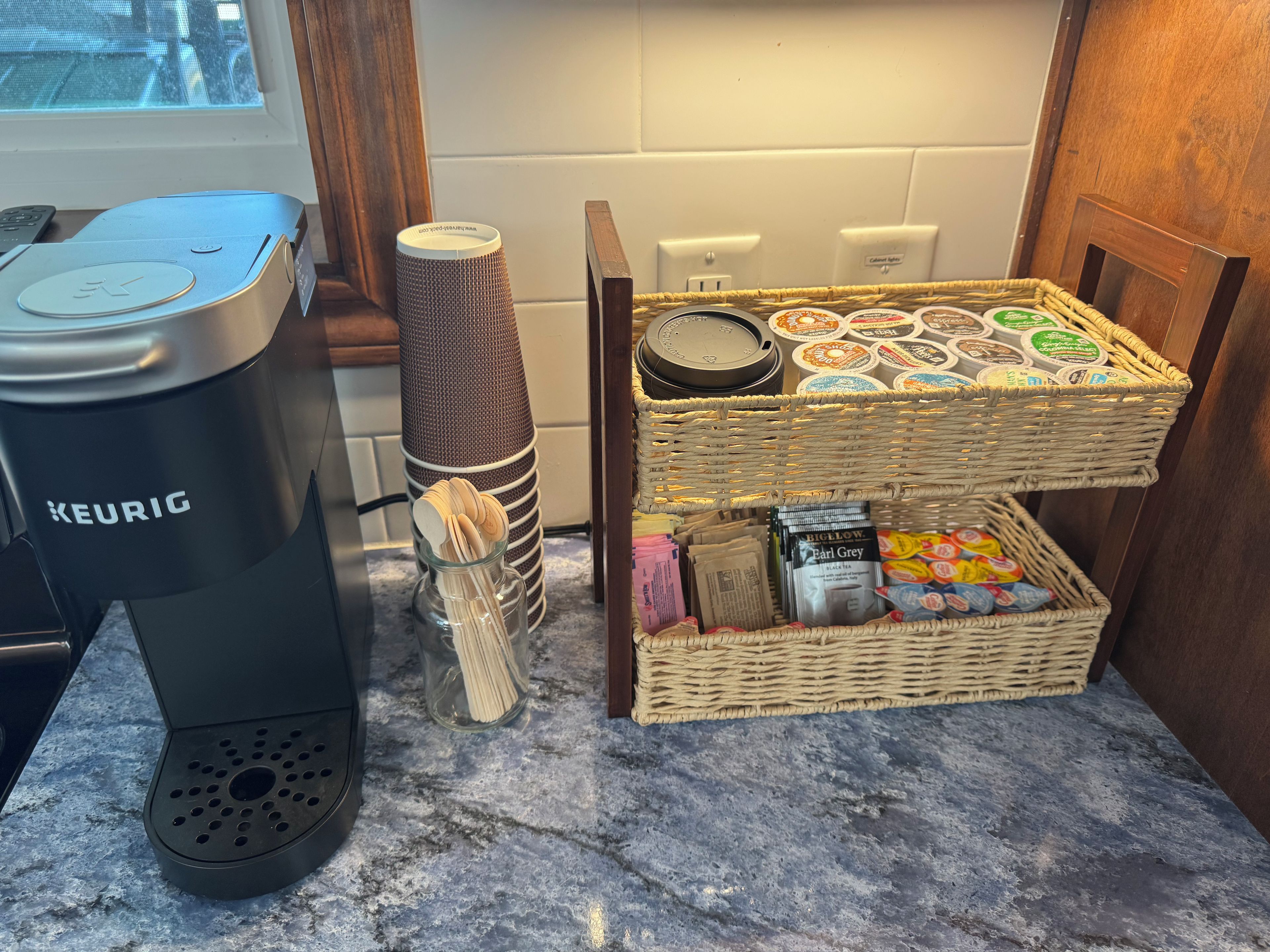 Een Keurig koffiezetapparaat, een mand met koffiekapsules en een houder met koffiefilters op een aanrecht.
