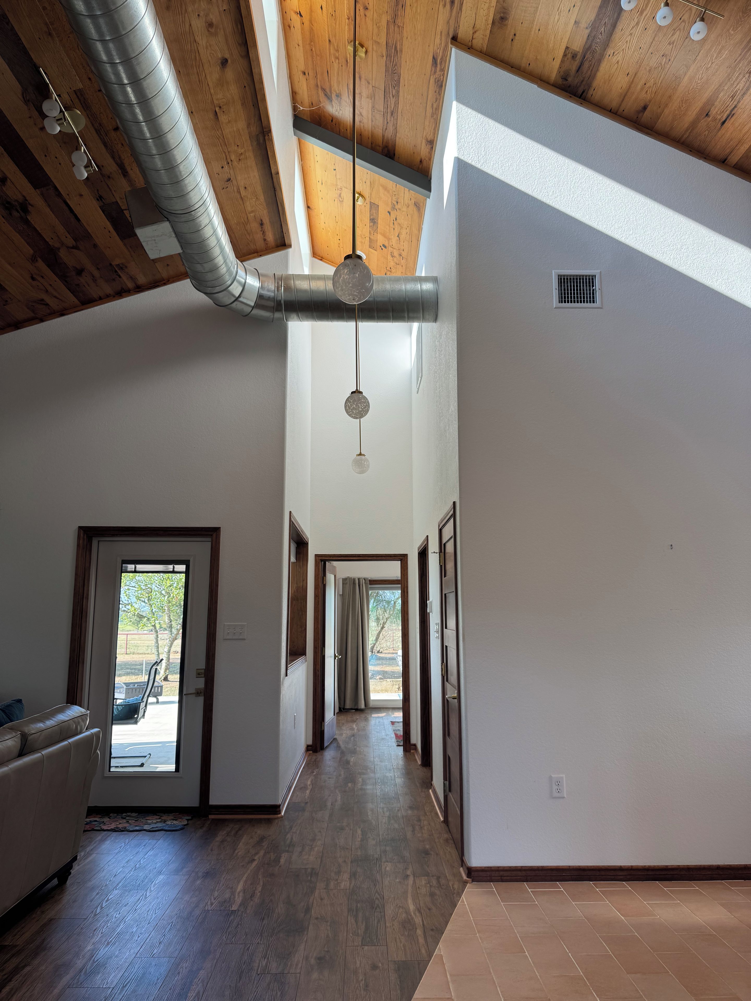 A spacious interior with a high ceiling, a central hallway, and a view through a door to an outdoor area.