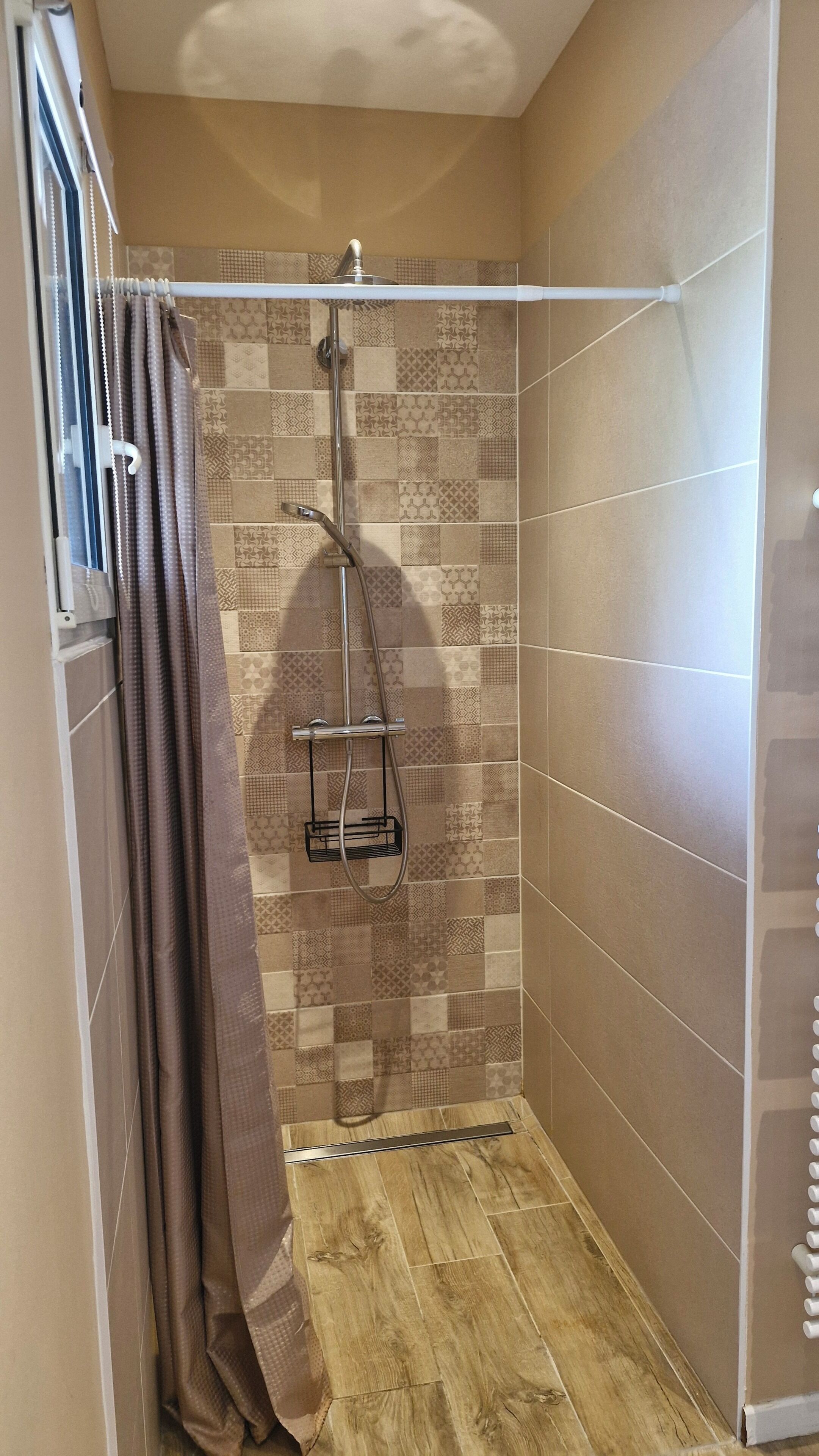 Een douche met een betegelde muur, een houten vloer en een gordijn.