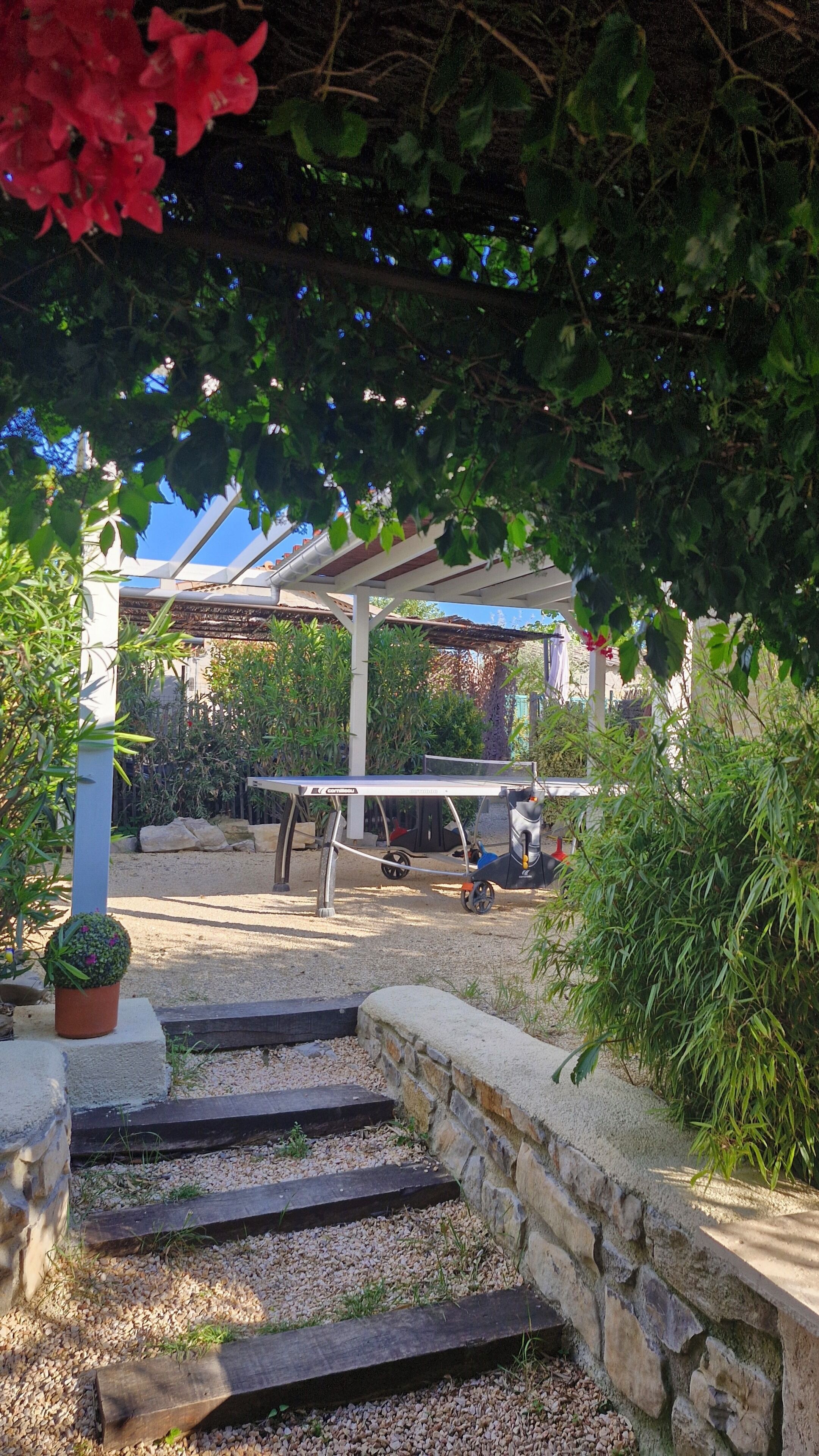 Een tuin met een pergola, een tafeltennistafel en een stenen muur.
