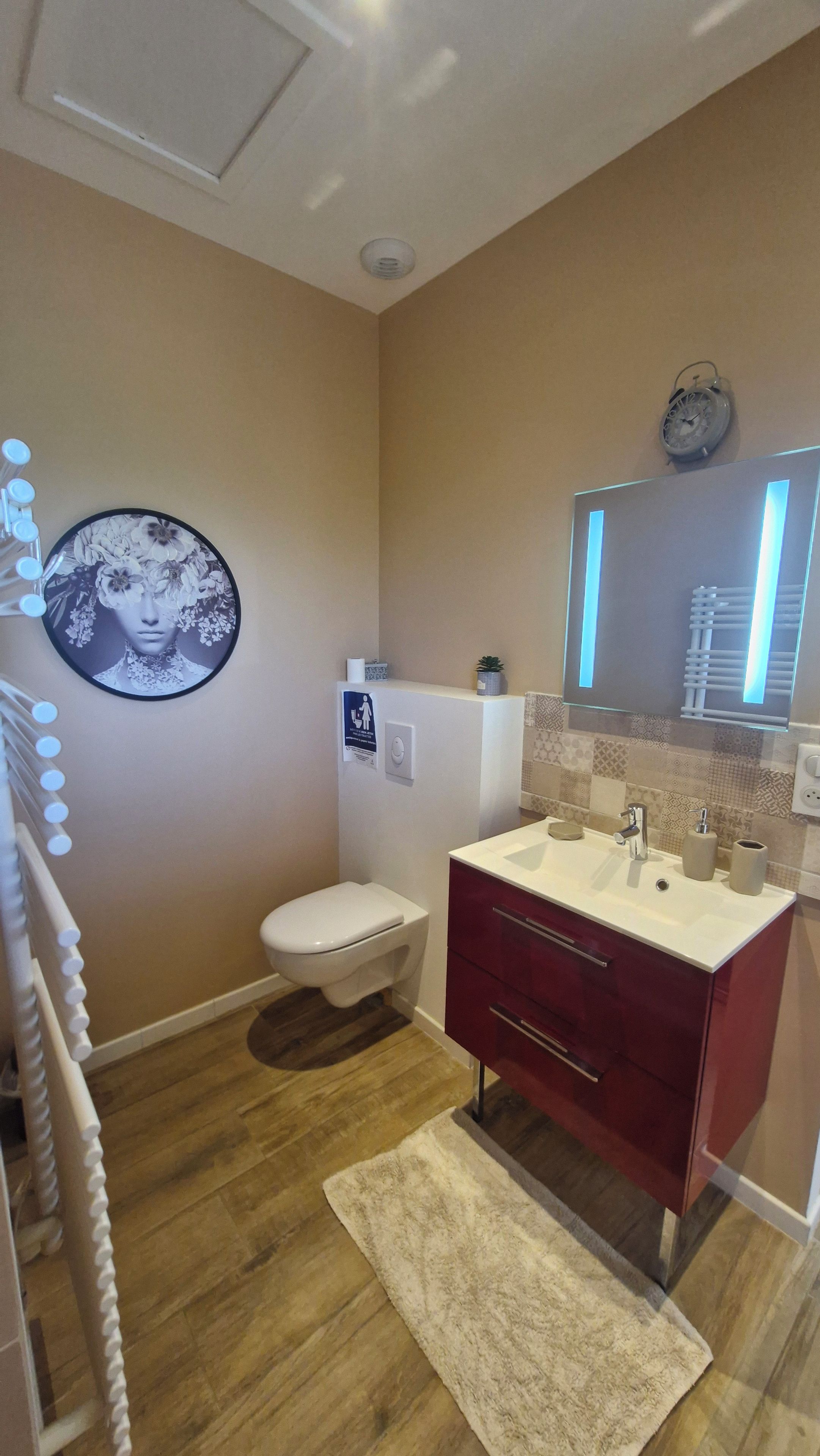 A bathroom with a toilet, sink, mirror, and a decorative wall piece.