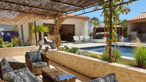 An outdoor seating area with wicker furniture, a pool, and a stone wall.