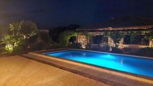 Une piscine dont le bord est revêtu de carreaux, entourée d’un espace paysager agrémenté de plantes et d’un bâtiment dont le toit est également recouvert de carreaux.