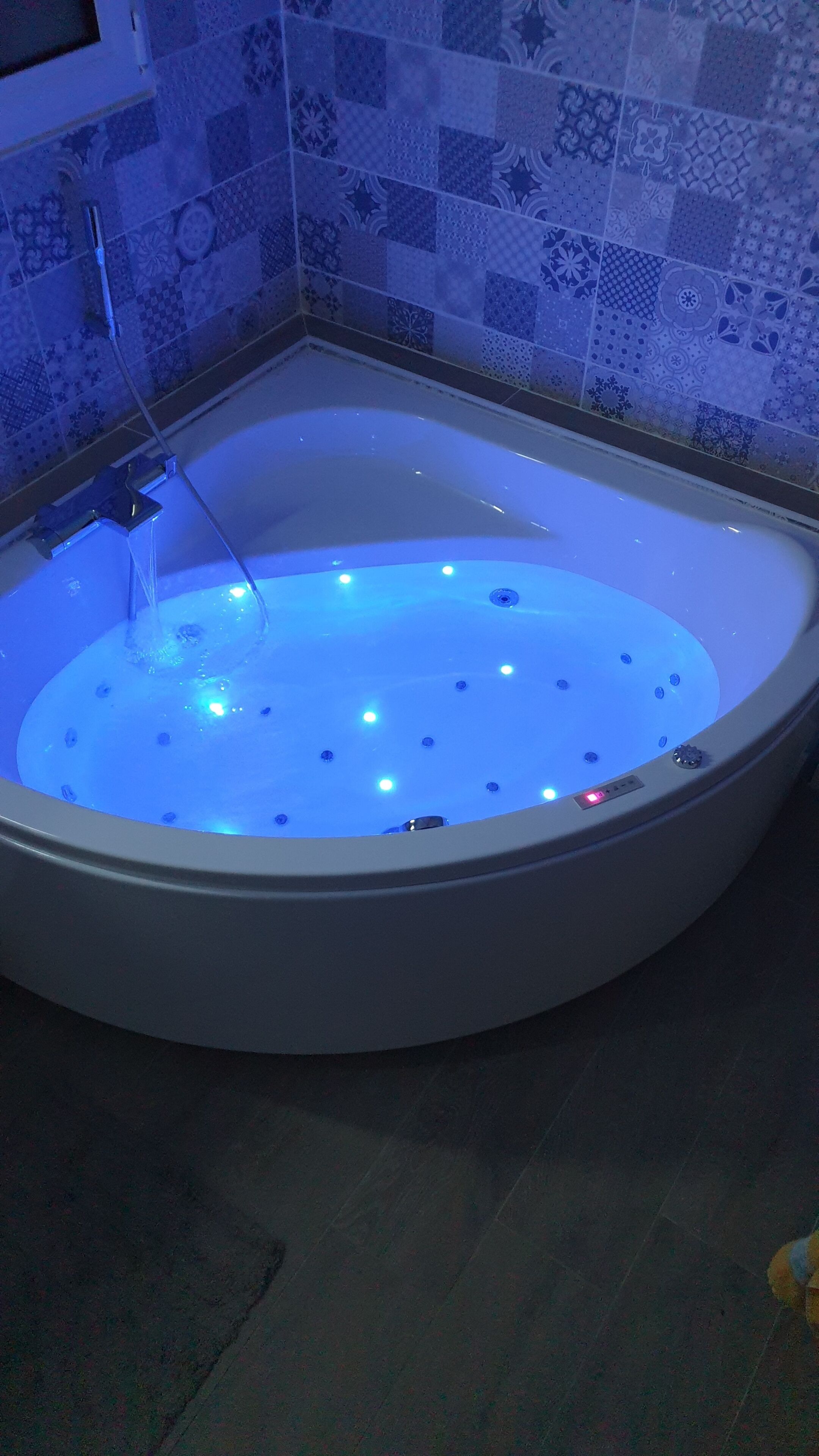 Une baignoire dotée d’un système d’éclairage bleu, d’une pomme de douche et d’un panneau de commande.