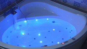 A bathtub with a blue light feature, a showerhead, and a control panel.