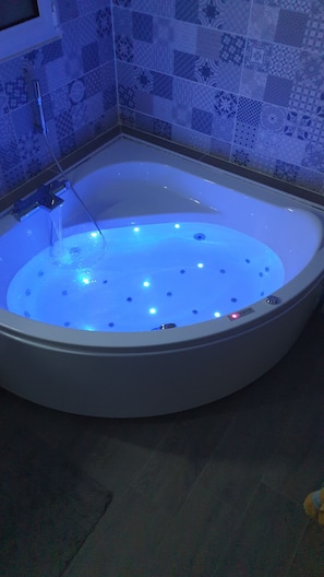 A bathtub with a blue light feature, a showerhead, and a control panel.