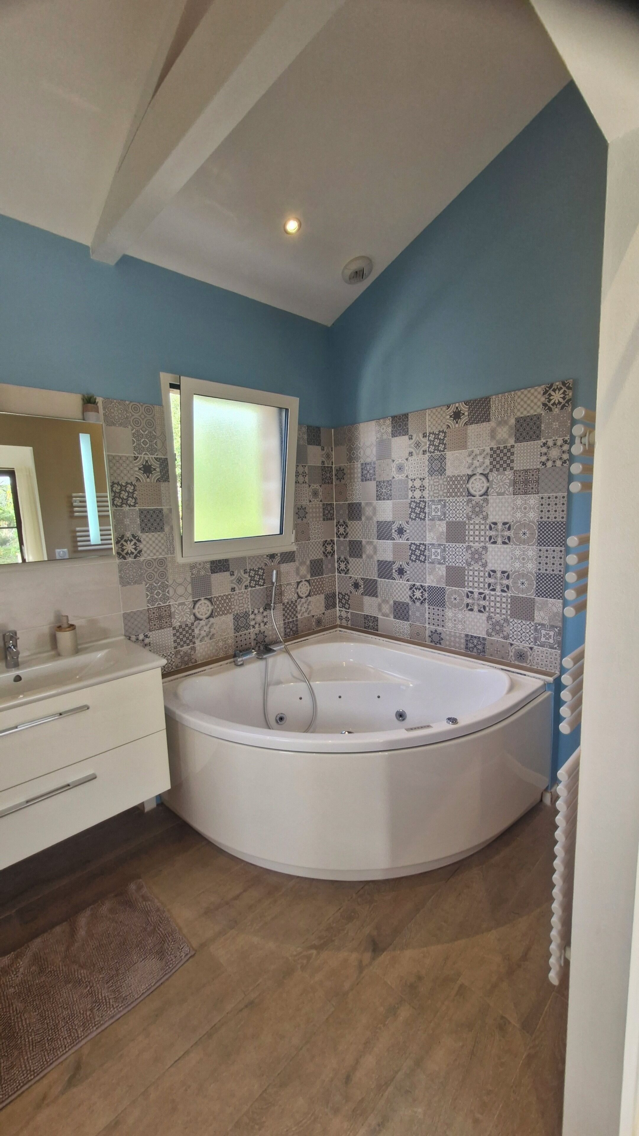 Une salle de bain avec une grande baignoire, un lavabo, un miroir et des carreaux décoratifs sur les murs.