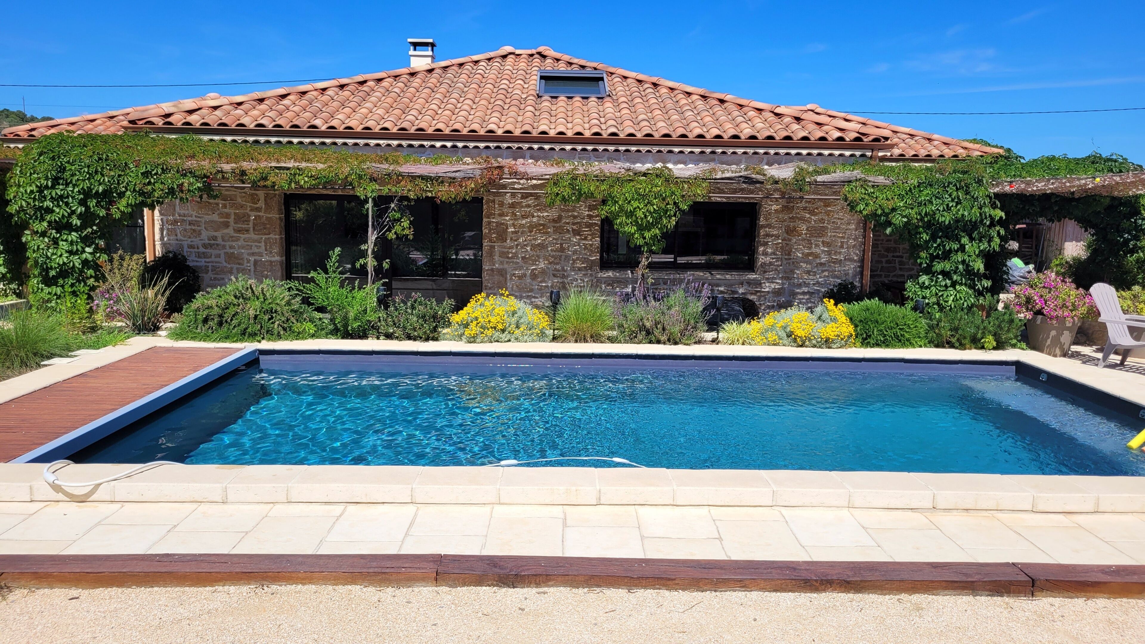 Une maison avec une piscine, des murs en pierre et un toit recouvert de tuiles.