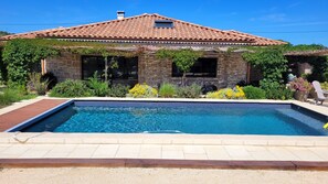 A house with a swimming pool, stone walls, and a tiled roof.