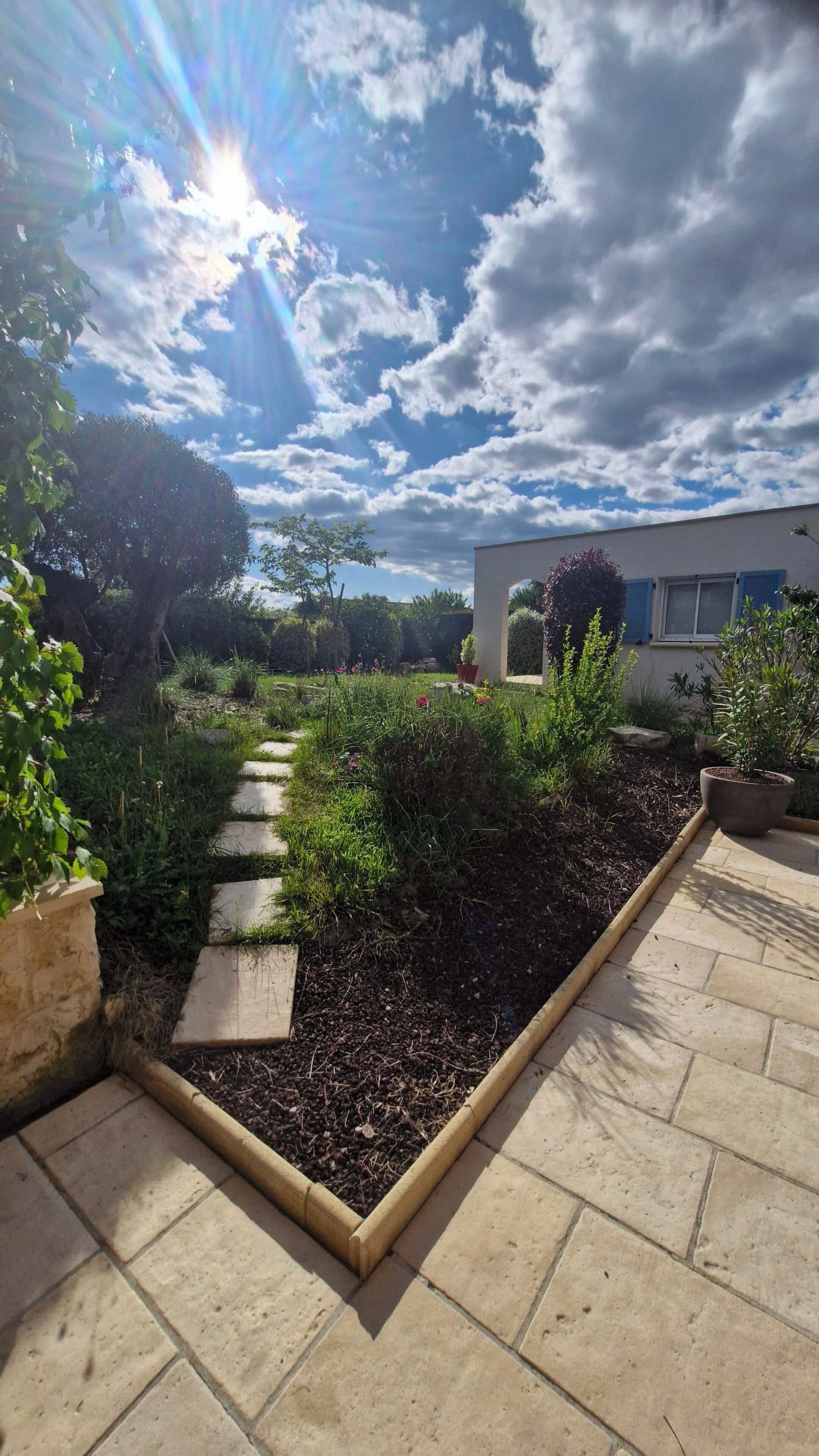 Un chemin de jardin qui mène à un bâtiment à la façade blanche et aux ornements bleus.