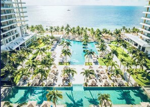 Resort com piscina central rodeada por espreguiçadeiras e palmeiras, com vista para um corpo de água.