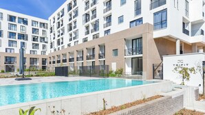 En modern byggnad med en swimmingpool, flera balkonger och en grind vid ingången.