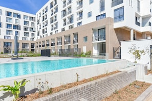Un immeuble moderne doté d’une piscine, de nombreux balcons et d’une entrée sécurisée.