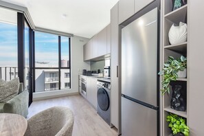 Une cuisine moderne équipée d’un lave-linge intégré, d’un grand réfrigérateur et d’un coin repas offrant une vue sur la ville.