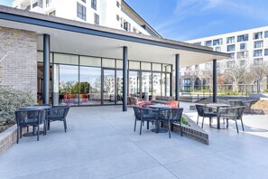 Un espace extérieur aménagé en terrasse, avec des tables et des chaises, un coin salon abrité et une vue sur les bâtiments environnants.