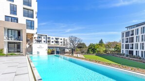 En modern byggnad med en swimmingpool, utomhusmöbler och en välskött gräsmatta.