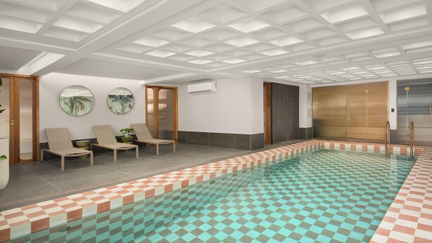 Ein Schwimmbecken mit Schachbrettfliesen, Liegestühlen und einer Decke mit Gittermuster.