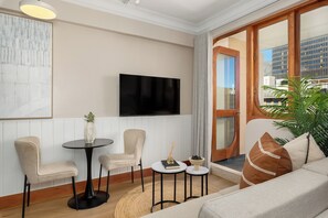 A modern living room with a flat-screen TV, two chairs, a small table, and a sofa. - Charlie and the Chairman | Urban Retreat (Cape Town)