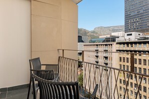 A balcony with two chairs and a table, overlooking a cityscape with buildings and mountains. - Charlie and the Chairman | Urban Retreat (Cape Town)