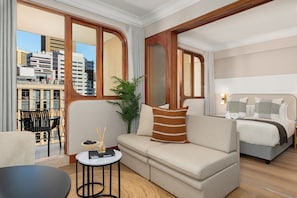 Habitación de hotel con sofá, una mesita, planta en maceta y cama con cabecera.
