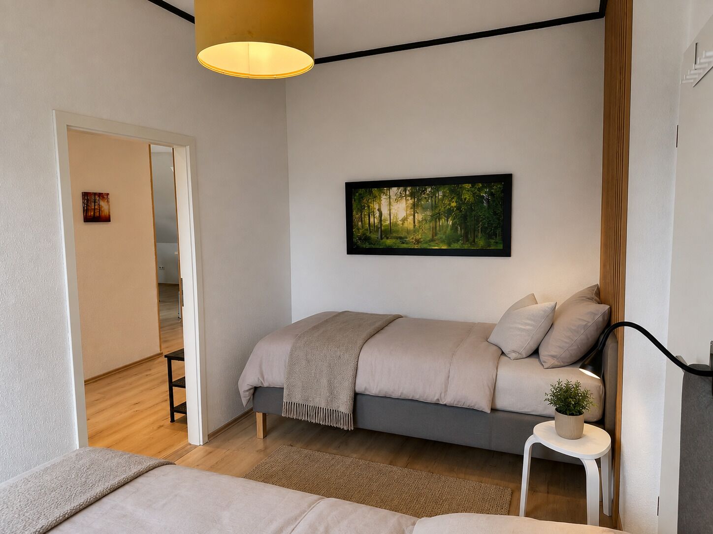 Ein modernes Schlafzimmer mit einem Bett, einem Gemälde, einem kleinen Tisch mit einer Pflanze und einer Treppe, die in ein anderes Zimmer führt.