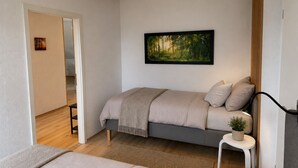 A modern bedroom with a bed, a painting, a small table with a plant, and a staircase leading to another room.