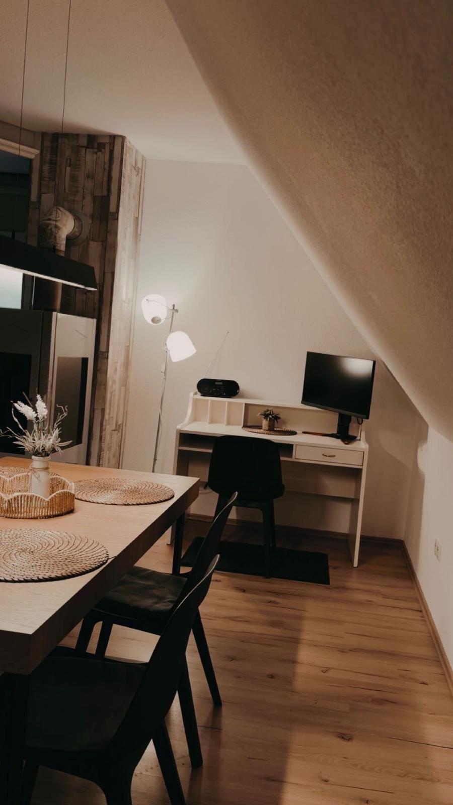 Een kleine kamer met een bureau, stoel en een tafeltje met een vaas.