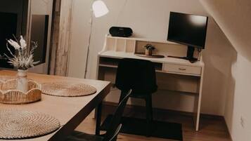 Een kleine kamer met een bureau, stoel en een tafeltje met een vaas.