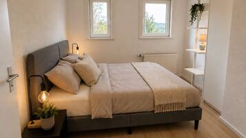 Een slaapkamer met een bed, bedlampen, een radiator en twee ramen.