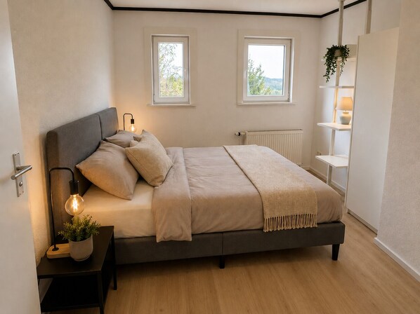 Une chambre à coucher avec un lit, des lampes de chevet, un radiateur et deux fenêtres.