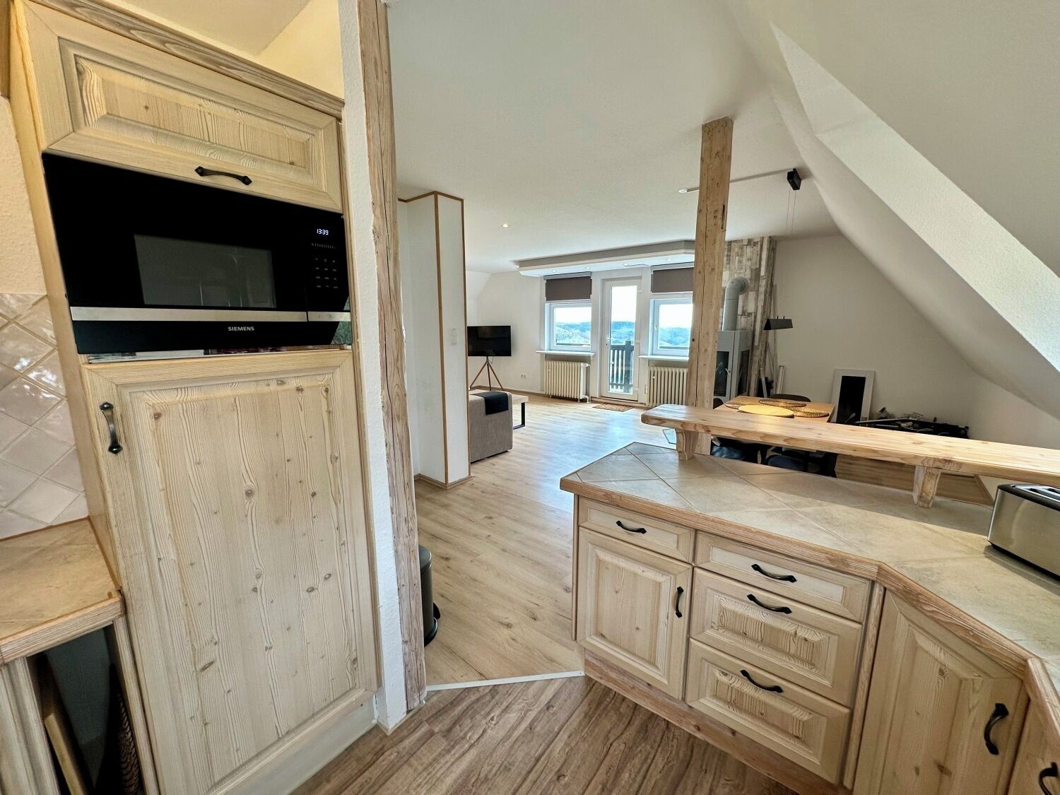 A modern kitchen with wooden cabinetry, a built-in microwave, and a large window providing natural light.