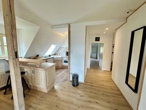 A modern kitchen with a wooden island, a dining area with a high ceiling, and a hallway leading to a bedroom.