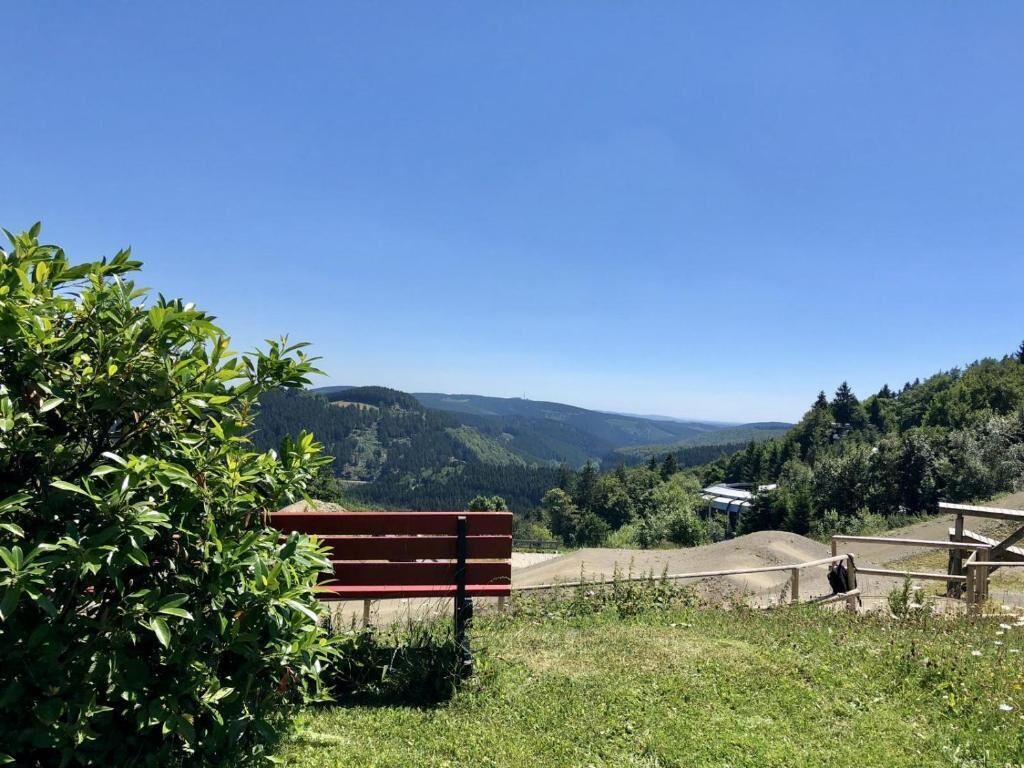 Eine Bank in einer grünen Umgebung mit freiem Blick auf eine hügelige Landschaft im Hintergrund.