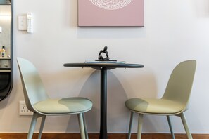 A room with a round table and two chairs, a wall-mounted light switch, and a framed picture above the table. - Charlie and the Chairman | City Views and Style (Cape Town)