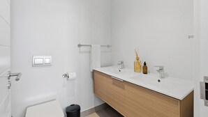 Un baño moderno con tocador blanco, dos lavamanos, un espejo y un inodoro.