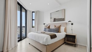 Un dormitorio moderno con una cama grande, una mesita de noche, una lámpara y vistas amplias a través de un ventanal.