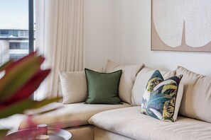 A modern living room with a sectional sofa, a green accent pillow, and a tropical patterned pillow. - Luxe 2xBR Apartment | Ocean Views | Aircon (Umhlanga)