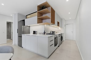 A modern kitchen with a central island, built-in appliances, and a mezzanine with wooden shelves. - Luxe 2xBR Apartment | Ocean Views | Aircon (Umhlanga)