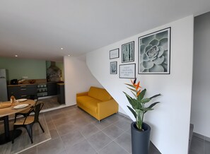 En moderne stue med spiseplads, en gul sofa og et køkken i baggrunden.