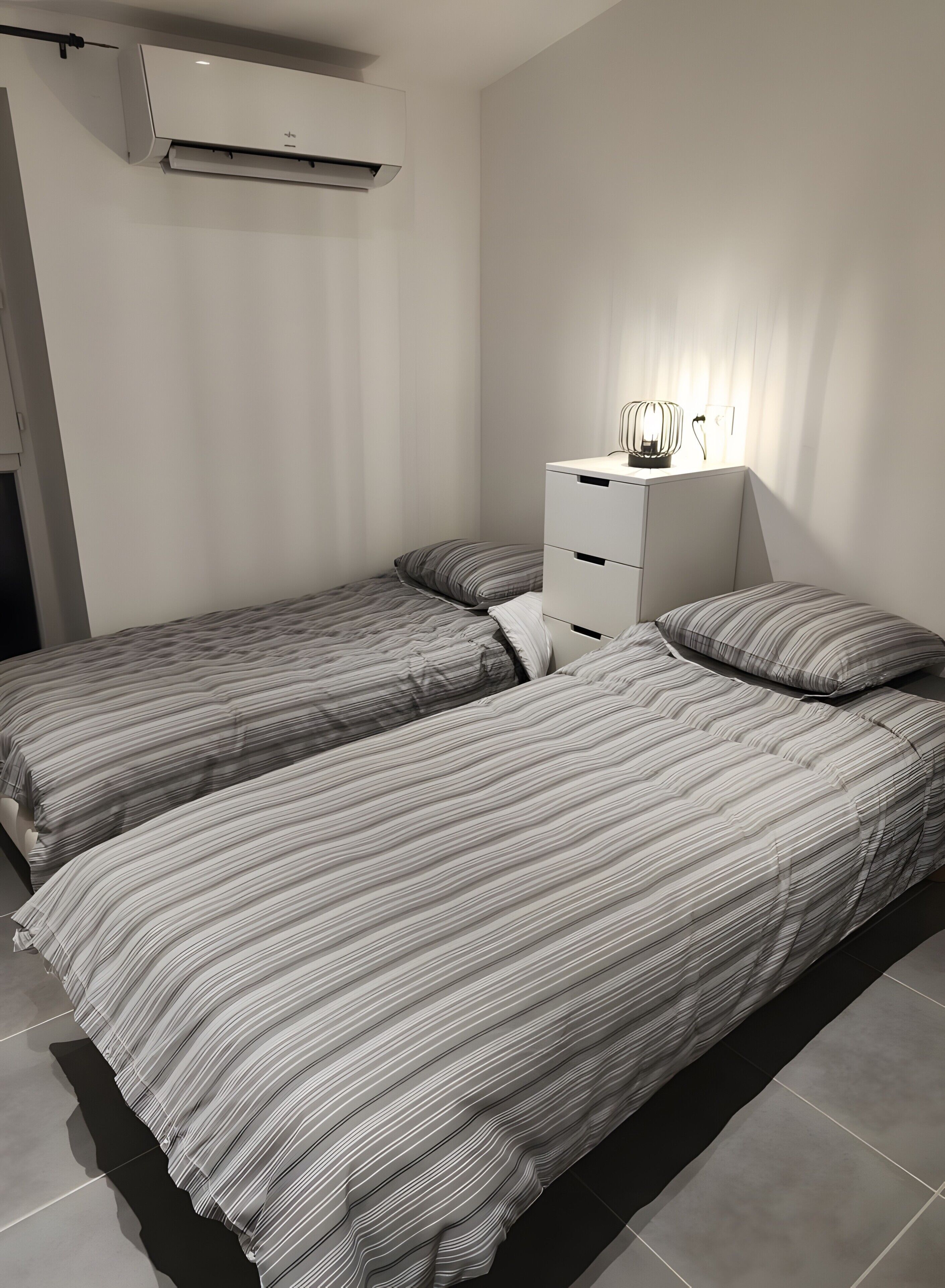 Een slaapkamer met twee bedden, een nachtkastje met een lamp en een airconditioner.