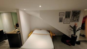 Une chambre d’hôtel avec un lit, un bureau, une chaise, une plante en pot et des œuvres d’art accrochées aux murs.