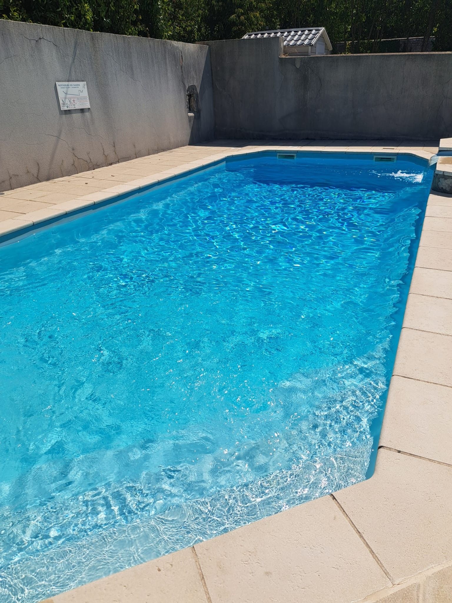 Une piscine rectangulaire à l’eau d’un bleu limpide, entourée d’une terrasse carrelée et d’un mur en béton.