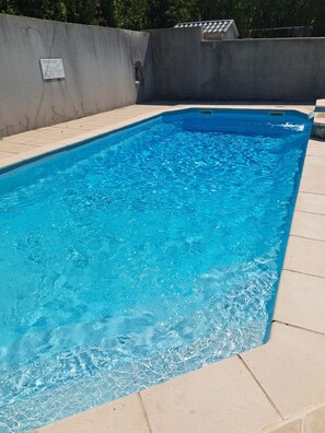 Una piscina rectangular con agua azul cristalina, rodeada por una solana con baldosas y una pared de hormigón.