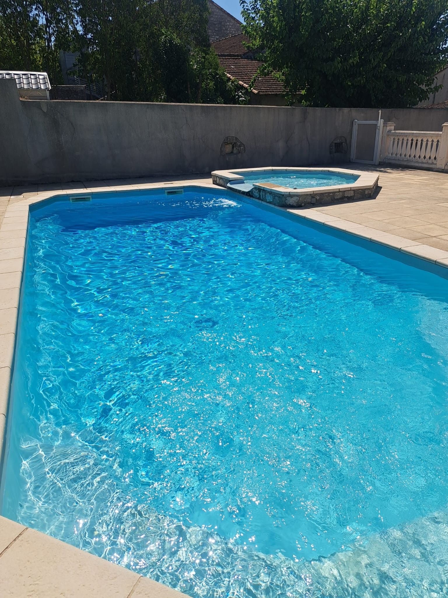 Een rechthoekig zwembad met een hottub ernaast, omgeven door een betonnen terras en een lage muur.