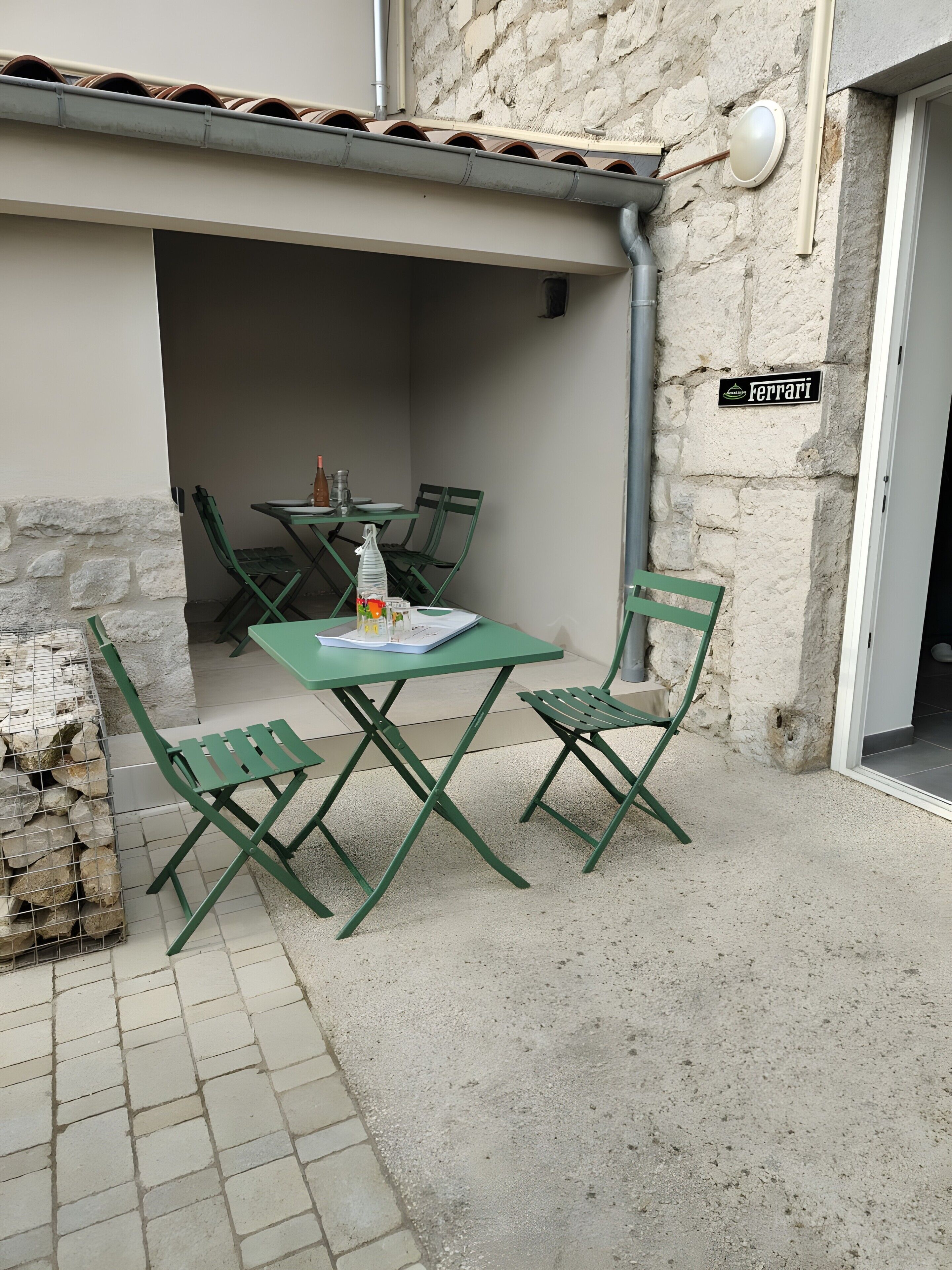 Un espace extérieur aménagé avec une table et des chaises, un mur en pierre et une enseigne sur laquelle on peut lire « Ferrari ».
